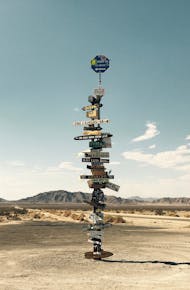 Tall signpost in a desert landscape under a clear blue sky with mountains in the background.