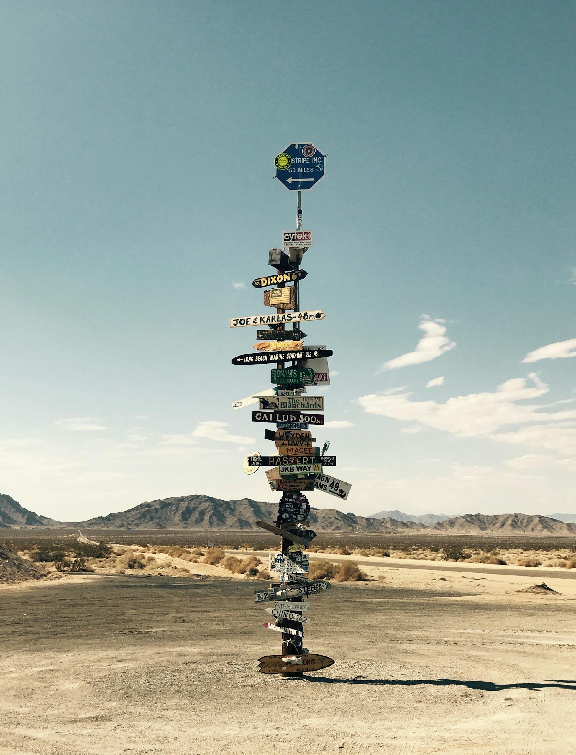 Tall signpost in a desert landscape under a clear blue sky with mountains in the background.