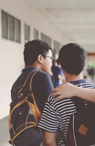 Group of male teenagers walking in a school corridor with backpacks, bonding and chatting.